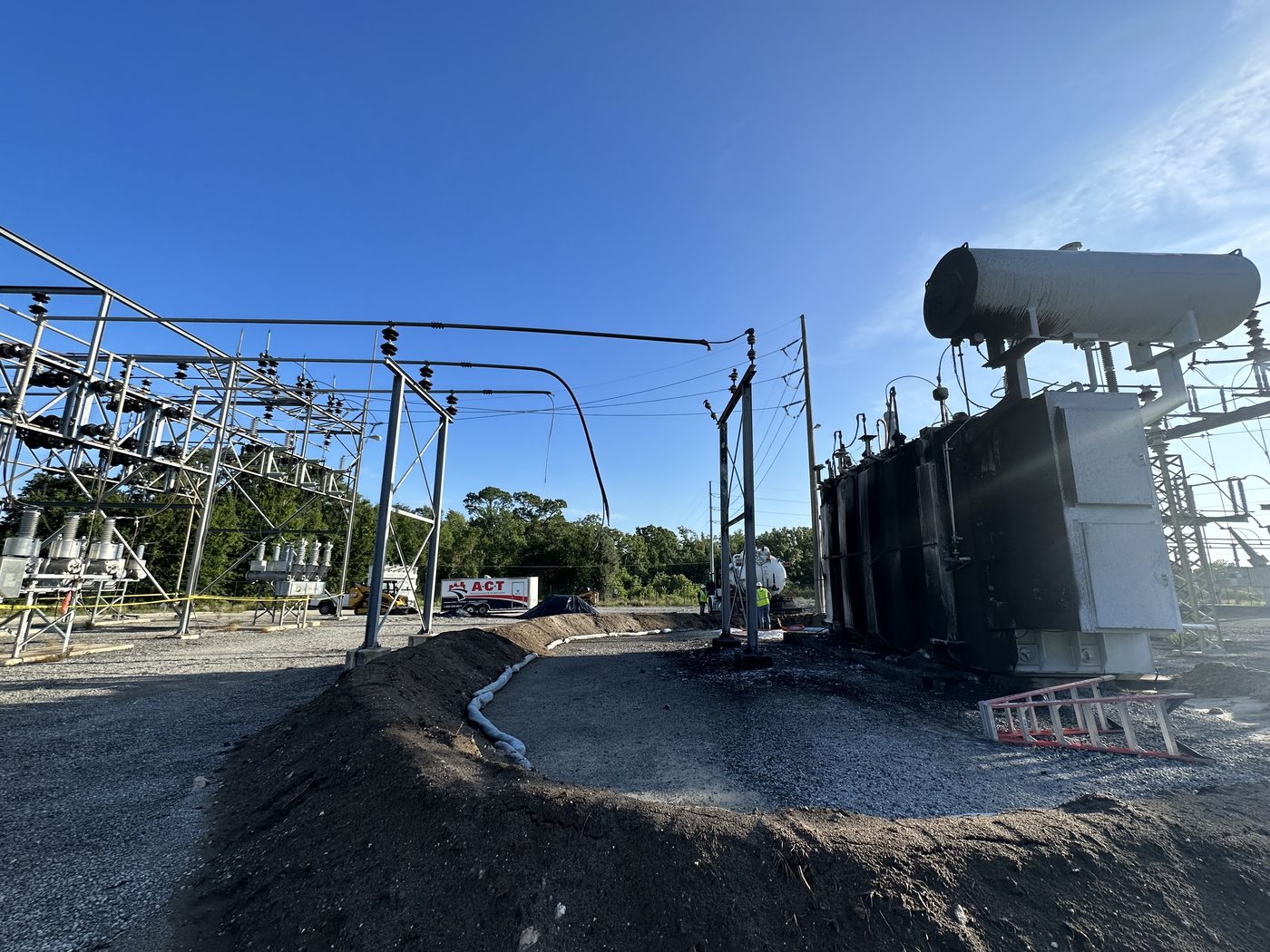 TECO 230 kV autotransformer failure site showing the replacement unit installed on the pad, scorched ground from the transformer fire, containment berms, and the bus structure that also required replacement.